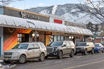 A row of SUVs are parked in front of a barber shop and a yoga studio at The Avenue Lofts Golden Apartments, Golden, Colorado at The Avenue Lofts Golden Apartments, Golden, Colorado